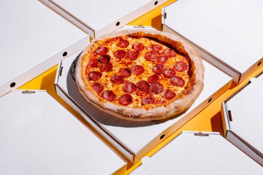Yeni pişmiş pepperonili pizza, etrafında birden fazla kutu bulunan bir pizza kutusunda oturur. Hepsi canlı sarı bir masanın üstüne yerleştirilir ve canlı bir atmosfer yaratır..