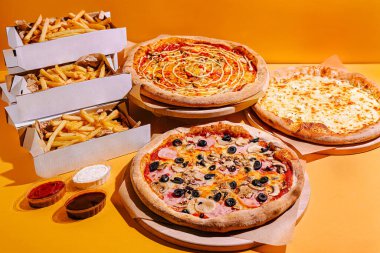 Üç farklı pizza çeşidi kızarmış patates ve sos yığınlarının yanında, arkadaşlarla ve ailelerle yemeklerin tadını çıkarmak için davetkar bir ortam yaratıyor..
