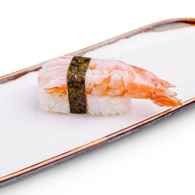 Pirinç tepeciğinin üzerine yerleştirilmiş karides soslu bir suşi. Beyaz dikdörtgen bir tabakta güzelce yerleştirilmiş bir yosun şeridiyle güvence altına alınmış..