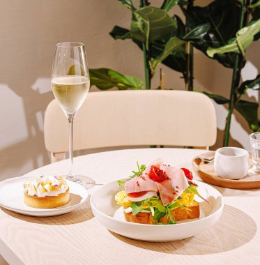 Brunch seti, üzerinde dilimlenmiş et ve sebzeler, yanında da bir tatlı ve bir bardak köpüklü içecek bulunan renkli bir tabak içeriyor. Sıcak bir atmosfer..