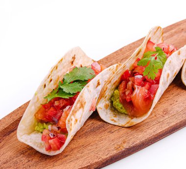 Domates, soğan ve kişniş gibi canlı malzemelerle dolu tacolar ahşap bir tahtaya güzelce yerleştirilmiş taze tatlar ve her yemek için mükemmel mutfak sanatları sergiliyorlar..