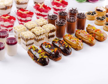 Pastalar, pastalar ve pudinglerin yer aldığı bir masada renkli bir dizi tatlı güzel bir şekilde düzenlenmiştir. Her biri vitrinlere canlı malzemeler ve kremalı dokular katıyor. Kutlama için mükemmel..