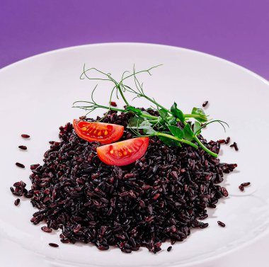 Tabakta parlak kırmızı domates dilimleri ve taze otlarla kaplı cömert bir siyah pirinç servisi yer alıyor. Renkli ve besleyici bir seçenek, sağlıklı bir yemek için ideal..