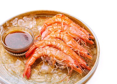 Plump, parlak turuncu karidesler küçük bir kase tuzlu sosun yanında buz dolu yuvarlak bir tabakta sıralanır. Deniz ürünleri taze ve keyifli görünüyor..