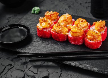 Bu yemek zevki, siyah bir tabakta düzgün sıralanmış canlı karidesli suşi rulolarını içeriyor. Soya sosu ve wasabi ile birlikte, iştah açıcı ve taze görünüyor..