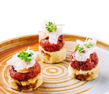 Üç küçük, karmaşık bir şekilde hazırlanmış aperatifler kırsal seramik bir tabakta sanatsal olarak düzenlenmiştir. Her yemeğin bir tabanı ve canlı bir üst tabakası var. Mutfak yaratıcılığını gösteriyor..