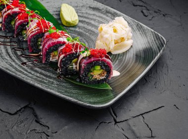 Taze malzemeler içeren suşi ruloları parlak, koyu bir tabakta güzelce düzenlenmiştir. Zirveler arasında canlı yumurta ve zarif süslemeler, mutfak sanatının sergilenmesi yer alıyor..