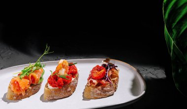 Modern bir tabakta ustalıkla hazırlanmış üç eşsiz bruschetta parçası. Her biri farklı malzemelere, taze malzemelere ve canlı renklere sahiptir. Mutfak deneyimi için mükemmeldir..