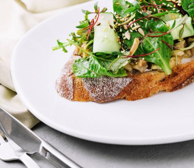 Beyaz bir tabakta roka, salatalık ve tohumla kaplı sağlıklı avokado tostu.