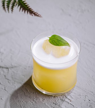 Zarif limon kokteyli nane yaprağıyla süslenmiş, eğreltiotu yapraklarının yanında dokulu bir yüzey üzerinde