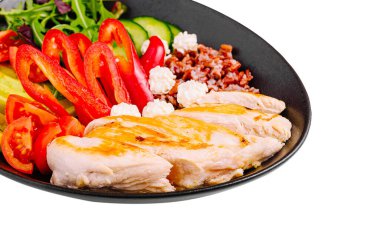 Canlı bir tabakta ızgara tavuk göğsü dilimleri ve yanında taze kırmızı biber, salatalık, yeşillik ve küçük peynir porsiyonları yer alıyor. Besleyici bir yemek için ideal..