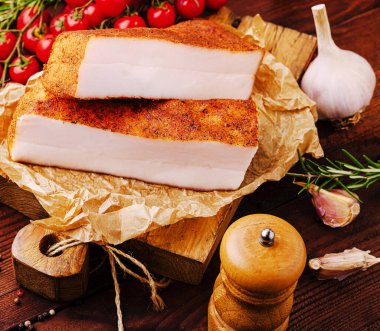 Taze sarımsak, kiraz domatesleri ve biberiye filizleriyle çevrili ahşap bir tahtada sergileniyor..