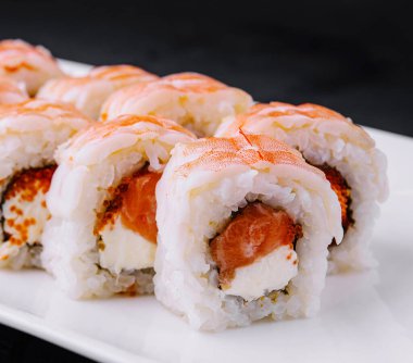 Beyaz bir tabakta somon ve pirinçli nefis suşi ruloları, siyah bir fona karşı.