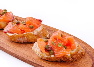 Tütsülenmiş somon ve kapari ile kaplı nefis şamdanlar ahşap bir tabakta dinleniyor.