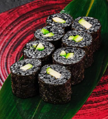 Siyah pirinç ile yapılan suşi ruloları yeşil sebzeler ve kremalı dolgu, canlı kırmızı bir tabakta güzelce düzenlenmiş, aşçılık yaratıcılığı ve sunum becerilerini sergiliyor.