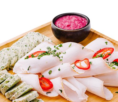 A wooden platter displays an assortment of sliced meats, fresh herbs, and diced tomatoes, accompanied by a small bowl of vibrant pink dip. The presentation emphasizes freshness and color. clipart