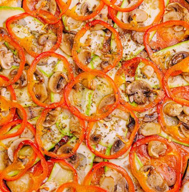 Yeni pişmiş bir pizza, bir toplanma ya da yemek için hazır, kırmızı biber, mantar ve ince dilimlenmiş sebzelerden oluşan canlı bir dizi sunar..