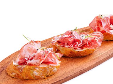 Pişmiş et dilimleriyle kaplı kabuklu ekmekle yapılan tuzlu bruschetta. Tabak ahşap bir tahtada sunuluyor, içeriğinin canlı renklerini ve dokularını sergiliyor..