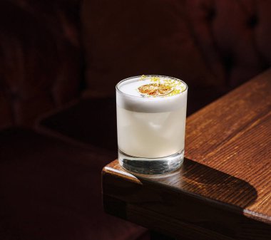 Kireç dilimli berrak bir kokteyl sıcak ışığın altında, ahşap bir masada duruyor. Sıcak atmosfer bir barda ya da dinlenme odasında rahatlama ve keyif öneriyor..