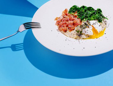 Özenle hazırlanmış brunch tabağında haşlanmış yumurta, kızarmış domuz pastırması ve sotelenmiş ıspanak yer alır.