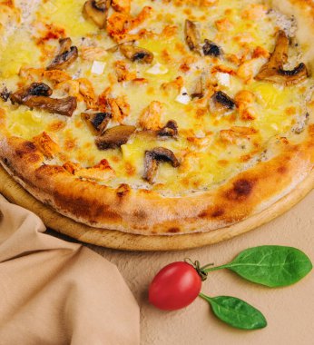 Tahta tabakta lezzetli bir tavuk ve mantarlı pizza, olgun bir domates ve fesleğen yaprağı.