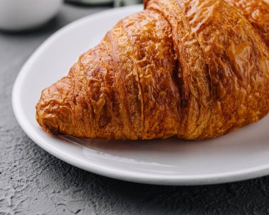 Beyaz bir tabakta yeni pişmiş bir kruvasanın yakın plan görüntüsü. Yumuşak dokusunu vurguluyor.