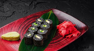 Çok güzel düzenlenmiş bir tabakta deniz yosunu, pirinç, salatalık ve avokado ile yapılmış suşi ruloları yer alır. Lezzetli bir yemek deneyimi için wasabi ve zencefil turşusu eşliğinde..