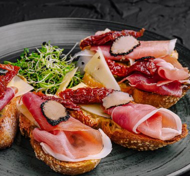 Çok güzel sunulmuş bir tost tabağı üzerinde çeşitli pişirilmiş etler, peynir ve güneşte kurutulmuş domatesler.