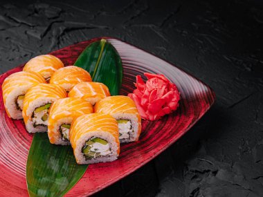 Çok güzel düzenlenmiş bir tabakta somonla kaplanmış birkaç suşi rulosu var. Canlı renkler turşulu zencefil ve dekoratif bir yaprak ile tamamlanıyor..