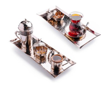 İki zarif gümüş tepside geleneksel bir çay bardağı ve tatlı ikramların yanında bir kahve demliği sergileniyor. Düzenlemede zengin bir kültürel içecek deneyimi sergileniyor.