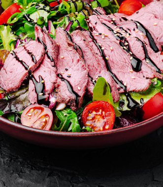 Karışık yeşillikler, kiraz domatesleri ve balzamik azaltımdan oluşan yumuşak et dilimlerinden oluşan canlı bir salata. Sağlıklı bir öğle ya da akşam yemeği için mükemmel..