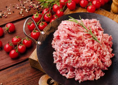 Zemin eti, ahşap bir yüzey üzerinde taze vişneli domateslerle çevrili siyah bir tabakta gösterilir. Yeşil biberiye güzel kokulu bir dokunuş ekliyor, canlı bir mutfak sahnesi yaratıyor..