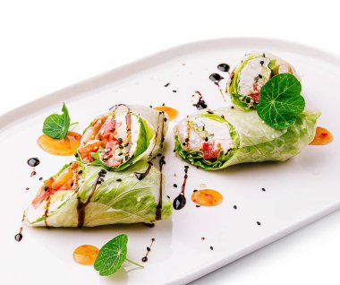 Taze sebzelerle dolu renkli marul ruloları ve beyaz bir tabağa serpiştirilmiş soslar sağlıklı bir yemek için mükemmel bir sunum oluşturur..