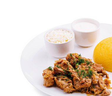 Lezzetli pişirilmiş et, beyaz bir tabakta servis edilen yumuşak pirinç ve yoğurdun yanında otlarla süslenmiş. Eğlenmeye hazır bir yemek..