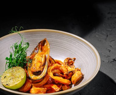 Zengin bir sosta servis edilen midye ve mürekkep balıklarıyla dolu canlı bir kase. Taze kireç ve bitkiler sunuma parlaklık katarak görsel olarak çekici hale getiriyor..