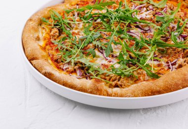 Lezzetli bir ton balığı ve beyaz tabakta roka pizza yakın plan.