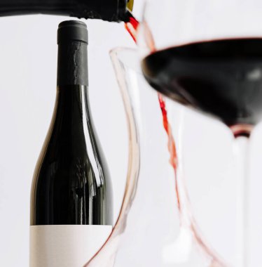 Şarap bardağa doldurulurken bir şişe kırmızı şarap masanın üzerine konur. Ortam minimalist, şarabın zengin rengini vurguluyor..