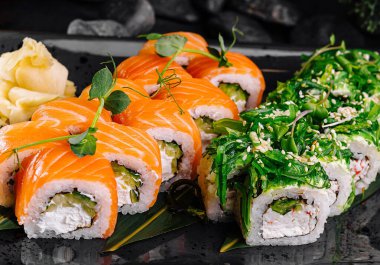 Soya sosuyla servis edilen, siyah bir tabakta somonla servis edilen zarif suşi rulo seçimi.