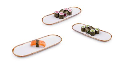 Üç zarif tepside somon nigiri, renkli rulo ve salatalık maki içeren çeşitli suşi türleri sergilenmektedir. Bu mutfak sunumu Japon mutfağının karmaşık detaylarını vurguluyor..