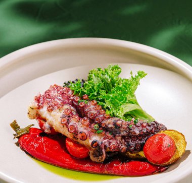 İçinde salatayla süslenmiş biber ve domateslerin de bulunduğu canlı sebzelerden oluşan bir yatakta ızgara ahtapot bulunan güzel bir tabak. Sunum aşçılık sanatını vurguluyor.