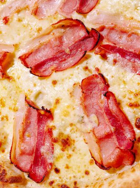 Eritilmiş peynir taze pişmiş bir pizza kabuğunu kaplar, çıtır pastırma şeritleriyle süslenir. Yemek davetkar ve servis edilmeye hazır görünüyor. Sıradan bir yemek ya da toplanma için mükemmel..