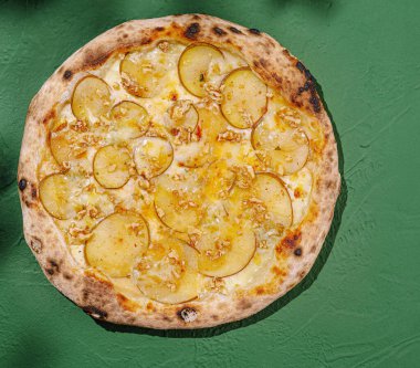 İnce dilimlenmiş patates, erimiş peynir ve kıtır fındıklı taze pişmiş pizza canlı yeşil bir yüzeye oturur. Eşsiz bir kombinasyon aşçılığa davetiye çıkarıyor..