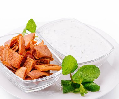 A bowl of crispy, golden-brown snacks sits next to a dish of creamy white dip. Fresh mint leaves garnish the plate, adding a pop of color to the tasty presentation. clipart