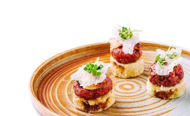 Three elegant appetizers are arranged on a stylish plate, featuring layers of minced meat, crispy elements, and garnishes. The presentation highlights culinary artistry and creativity. clipart