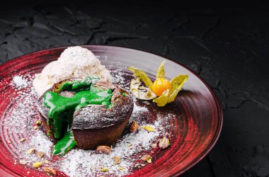 Bir tatlı tabağı, yeşil sosla ıslatılmış yapışkan erimiş bir kek sergiliyor, yanında da bir kepçe kremalı dondurma servis ediliyor. Altın böğürtlen ve ezilmiş fındıkla süslenmiş..