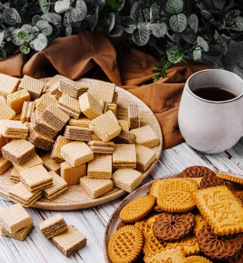 Bir fincan kahveyle tamamlanmış, ahşap tabaklar üzerinde düzgünce dizilmiş çeşitli kurabiye ve gofretlerden oluşan enfes bir ziyafet. Afiyet olsun..