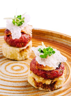 İki güzel sunulmuş gurme tartar, çıtır çıtır kabuklara istiflenmiş, mikro yeşillikler ve hassas malzemelerle süslenmiş. Bu yemek, aşçılık yaratıcılığını doku ve lezzet yoluyla sergiliyor..