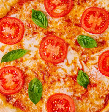 Yakın çekimde olgun domates dilimleri ve yeşil fesleğen yapraklarıyla süslenmiş peynirli pizza sergileniyor. Sıcak eritilmiş peynir malzemelerin canlı renklerini tamamlayarak davetkar bir yemek yaratıyor..