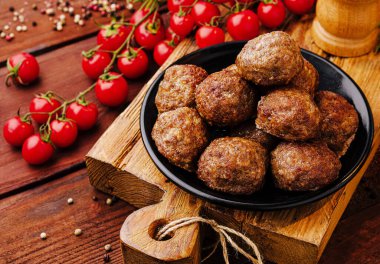 Canlı vişneli domateslerle çevrili ahşap bir tahtaya bir kase lezzetli köfte konur. Bu ağız sulandırıcı yemek lezzet ve tazeliği davet eder, paylaşmak için mükemmeldir..