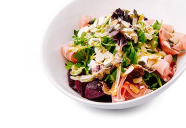 Canlı bir salatada karışık sebzeler, ince dilimler ve çeşitli fındıklar bulunur. Tabak bir tutam süsle süslenmiş, taze ve sağlıklı malzemeler sergileniyor..